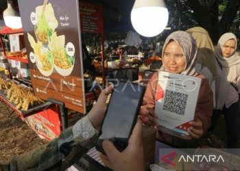 Pedagang melayani konsumen yang memindai kode sistem pembayaran Quick Response Code Indonesian Standard (QRIS) saat berbelanja di gerai kuliner Pesta Rakyat, Banda Aceh, Aceh, Jumat (26/7/2024). (ANTARA FOTO/Khalis Surry)