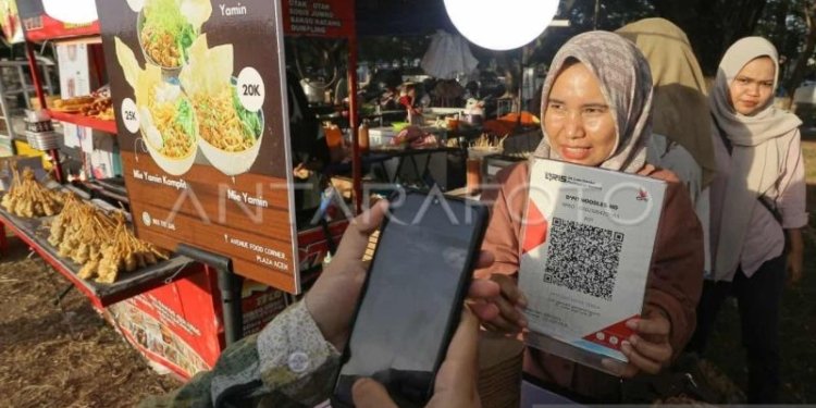 Pedagang melayani konsumen yang memindai kode sistem pembayaran Quick Response Code Indonesian Standard (QRIS) saat berbelanja di gerai kuliner Pesta Rakyat, Banda Aceh, Aceh, Jumat (26/7/2024). (ANTARA FOTO/Khalis Surry)